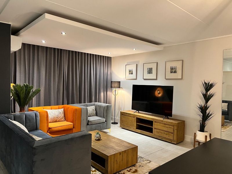 A well-maintained living room featuring tiled flooring, a modern recessed ceiling with integrated downlights, and a wall-mounted air conditioning unit.