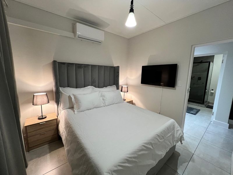 A well-maintained bedroom featuring tiled flooring, a wall-mounted air conditioning unit, and direct access to an en-suite bathroom.