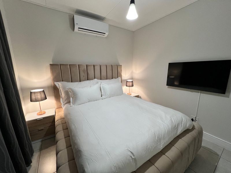 A well-maintained bedroom featuring tiled flooring, a wall-mounted air conditioning unit, and a wall-mounted television.
