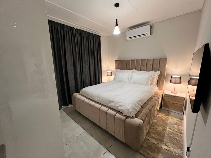 A well-maintained bedroom featuring tiled flooring, a wall-mounted split-system air conditioner, and modern pendant lighting.