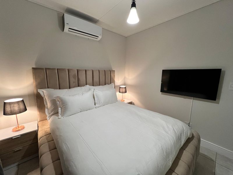 A well-maintained bedroom featuring a wall-mounted air conditioning unit, tiled flooring, and a wall-mounted television.