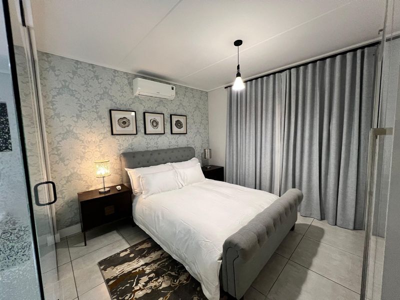 A well-maintained bedroom featuring tiled flooring, a split-system air conditioner, and neutral wall finishes with floor-to-ceiling curtains.