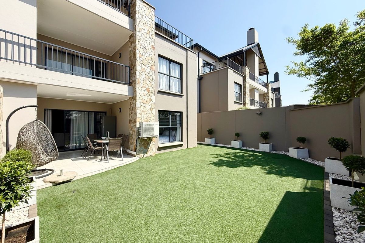A well-maintained rear exterior featuring a covered patio, artificial lawn, and stone-clad architectural details, providing a private outdoor living space.