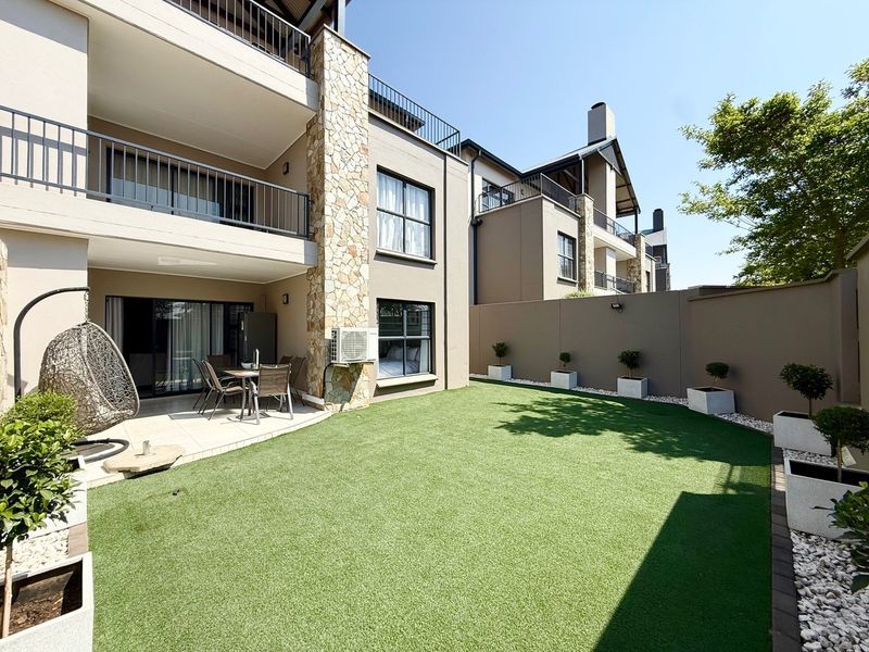 A well-maintained rear exterior featuring a covered patio, artificial lawn, and stone-clad architectural details, providing a private outdoor living space.