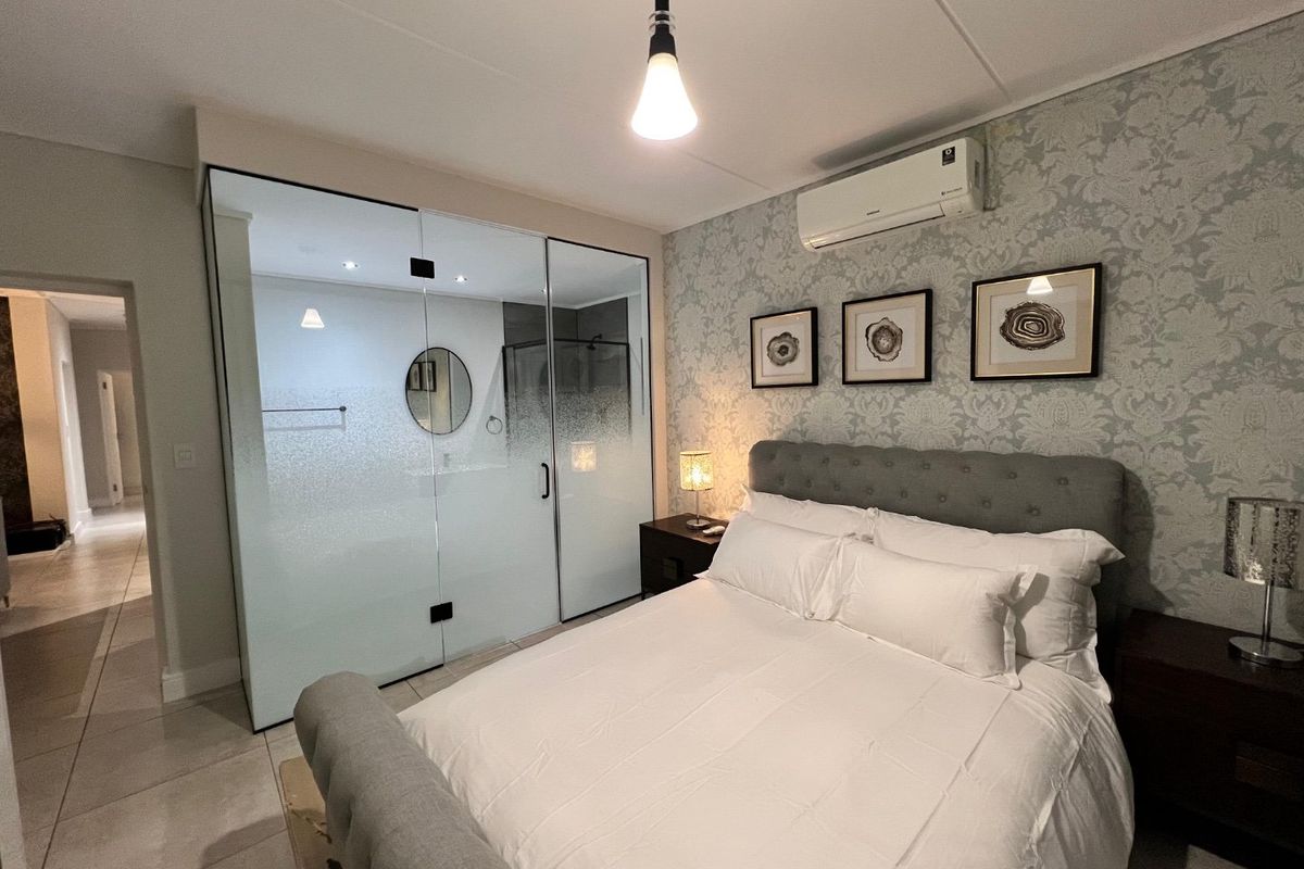 Modern bedroom featuring a unique glass-enclosed en-suite bathroom, tiled flooring, split-system air conditioning, and elegant wallpaper accent wall.