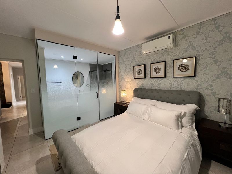 Modern bedroom featuring a unique glass-enclosed en-suite bathroom, tiled flooring, split-system air conditioning, and elegant wallpaper accent wall.