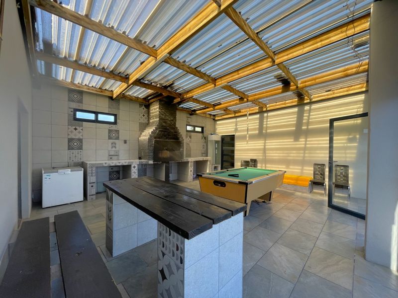 Covered outdoor entertainment area featuring a built-in braai, tiled surfaces, and a timber-framed corrugated roof, ideal for social gatherings.