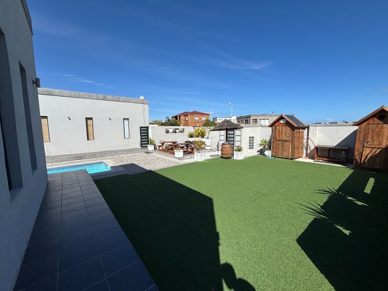 Spacious rear garden featuring a swimming pool, artificial lawn, paved patio area, and perimeter boundary walls.