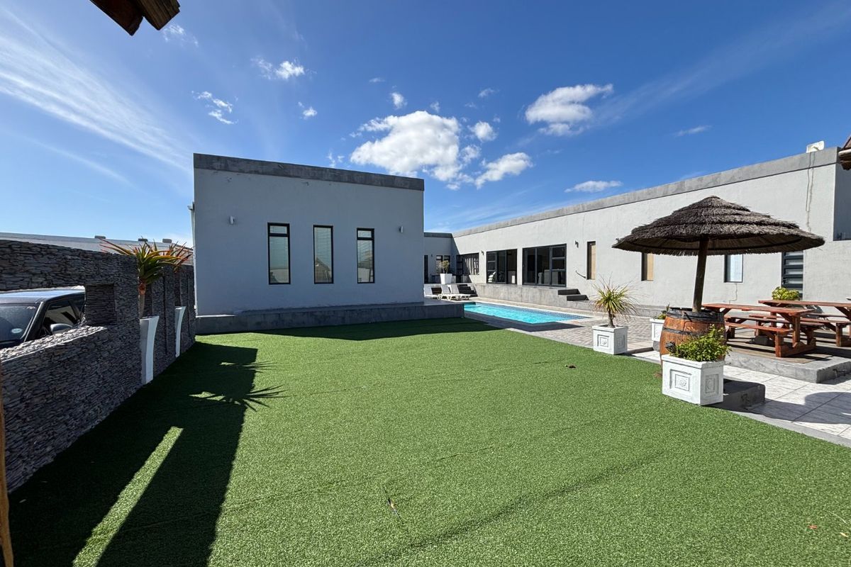 A well-maintained rear courtyard featuring an artificial grass lawn, a swimming pool, and stone-clad boundary walls, providing a clean outdoor entertainment space.