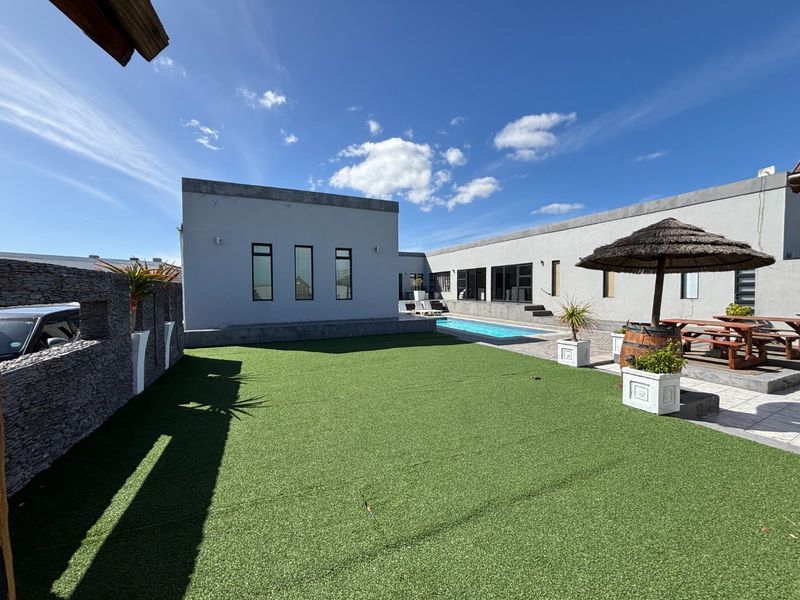 A well-maintained rear courtyard featuring an artificial grass lawn, a swimming pool, and stone-clad boundary walls, providing a clean outdoor entertainment space.