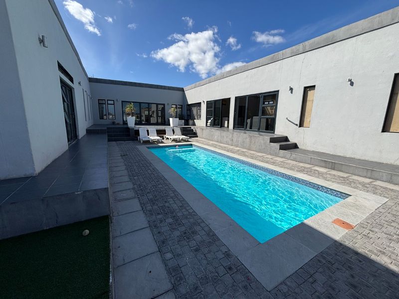 A modern courtyard featuring a rectangular swimming pool, paved surround, and direct access to the home through multiple sliding glass doors.