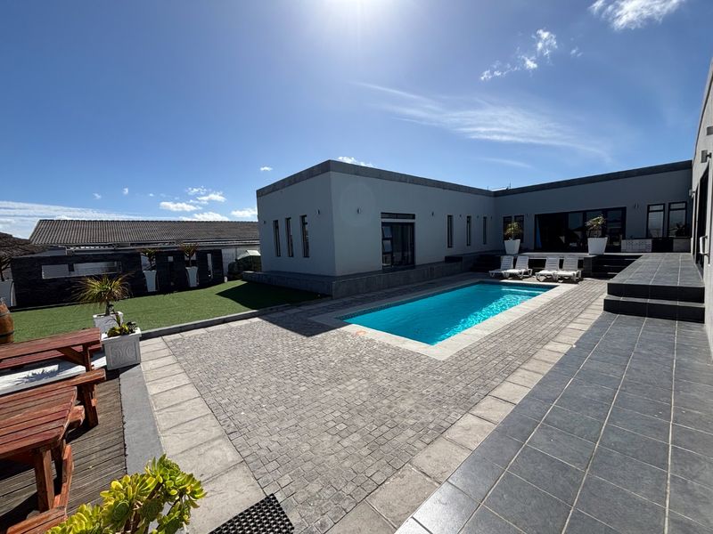 A well-maintained outdoor pool area featuring a swimming pool, paved patio, tiled terrace, and artificial lawn, ideal for outdoor entertaining.
