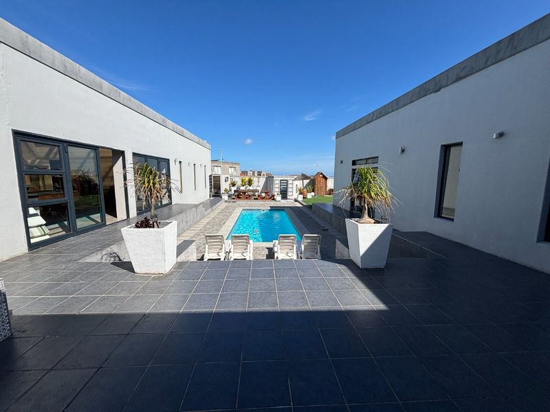 A modern courtyard featuring a central swimming pool flanked by tiled patio areas and large sliding glass doors providing seamless indoor-outdoor flow.