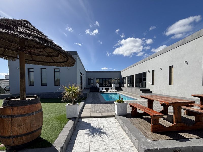 A spacious outdoor courtyard featuring a swimming pool, paved patio area, and artificial lawn, surrounded by the property's exterior walls.