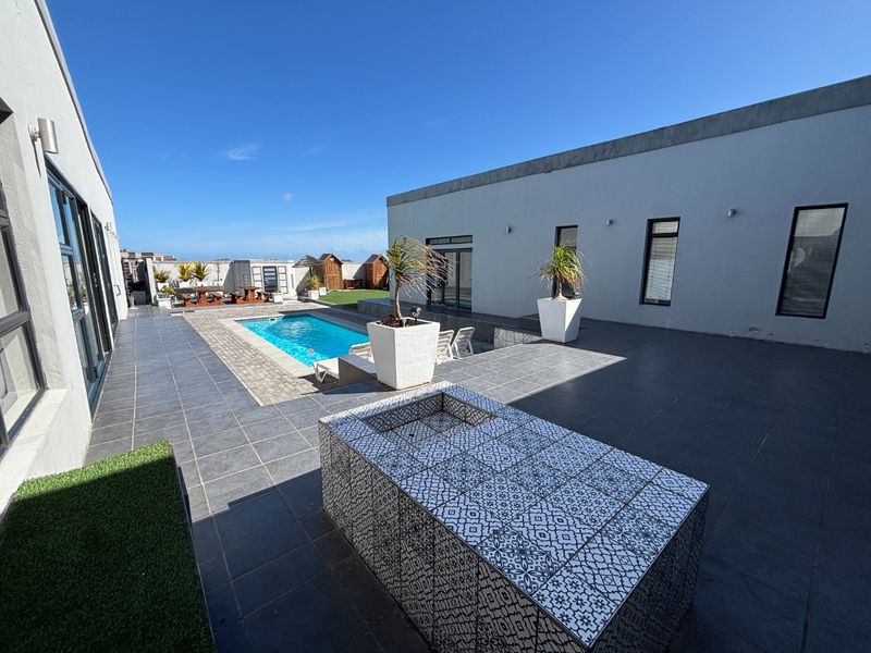 Spacious outdoor entertainment area featuring a swimming pool, large tiled patio, and a decorative built-in braai station.