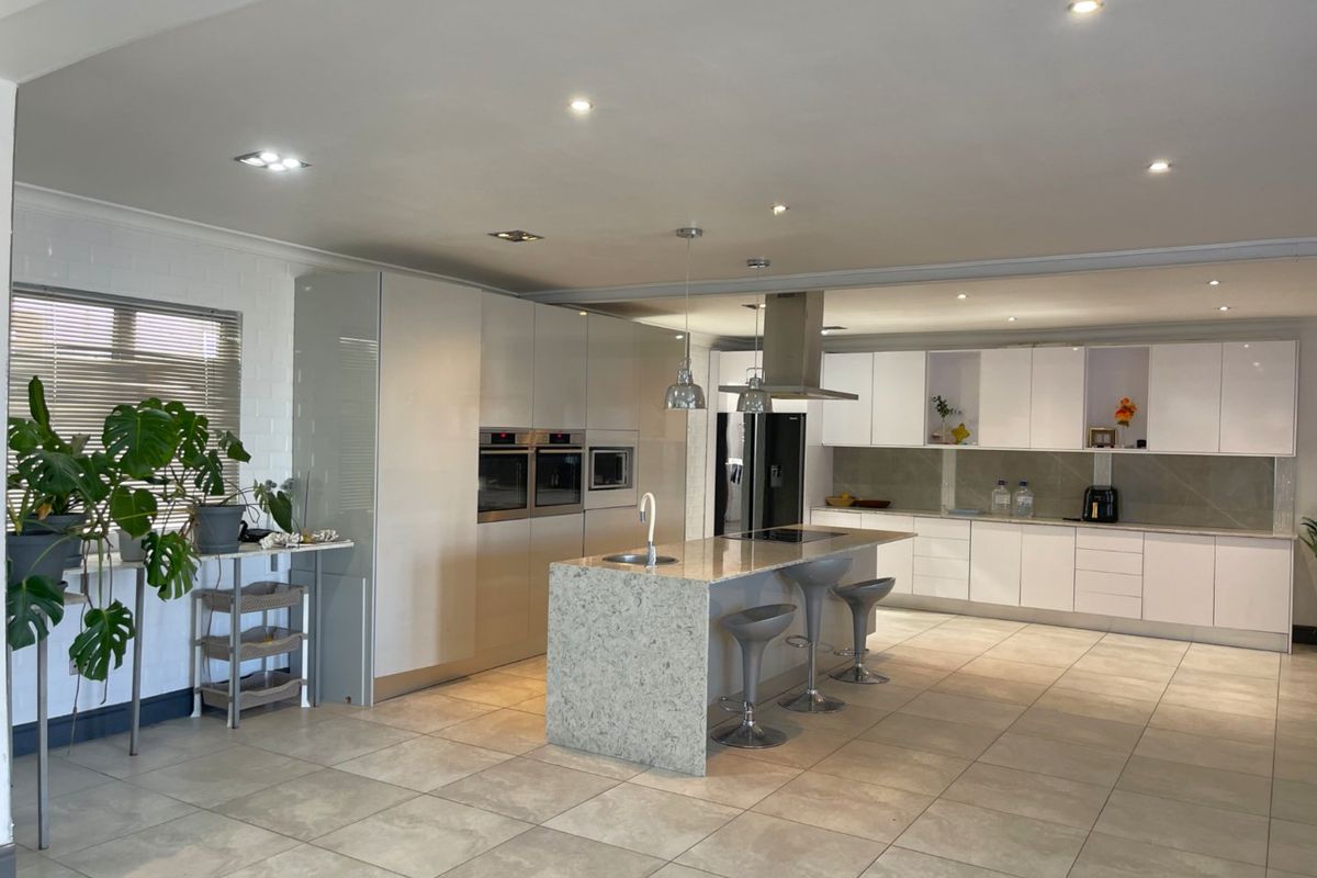 Modern open-plan kitchen featuring sleek white cabinetry, stone countertops, a central island with sink, and integrated built-in appliances.
