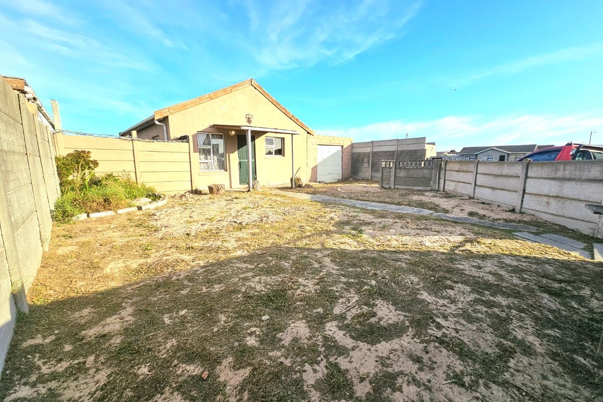 Rear exterior view of the property featuring a modest yard, precast concrete boundary walls, and a single garage door.