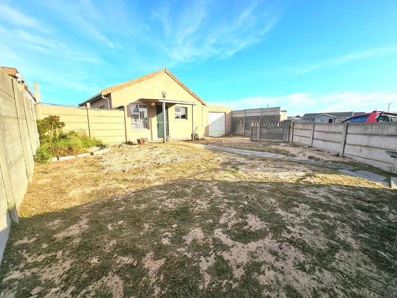Rear exterior view of the property featuring a modest yard, precast concrete boundary walls, and a single garage door.
