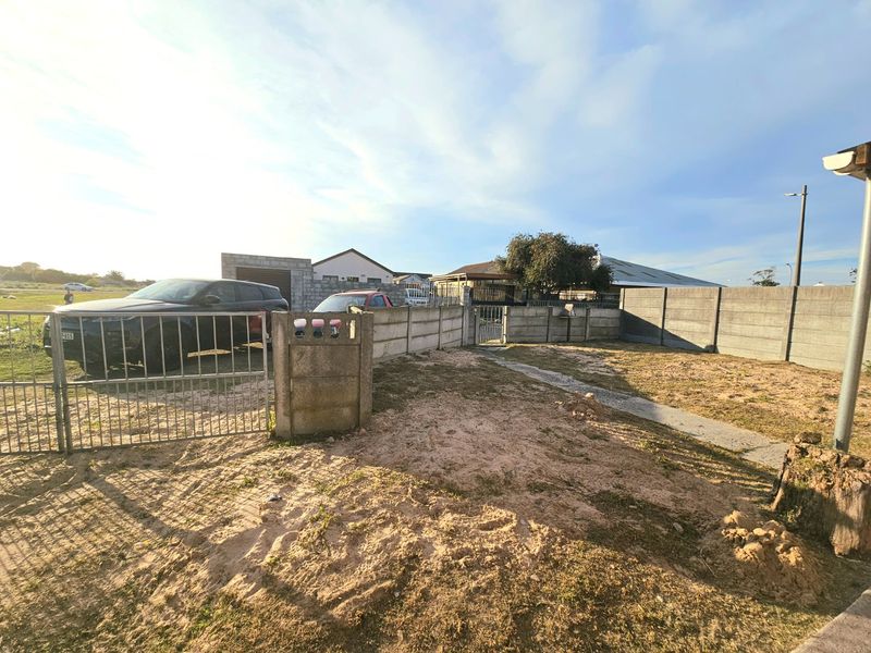 Front exterior view of the property featuring a metal gate, precast concrete boundary wall, and an unlandscaped sandy yard area.