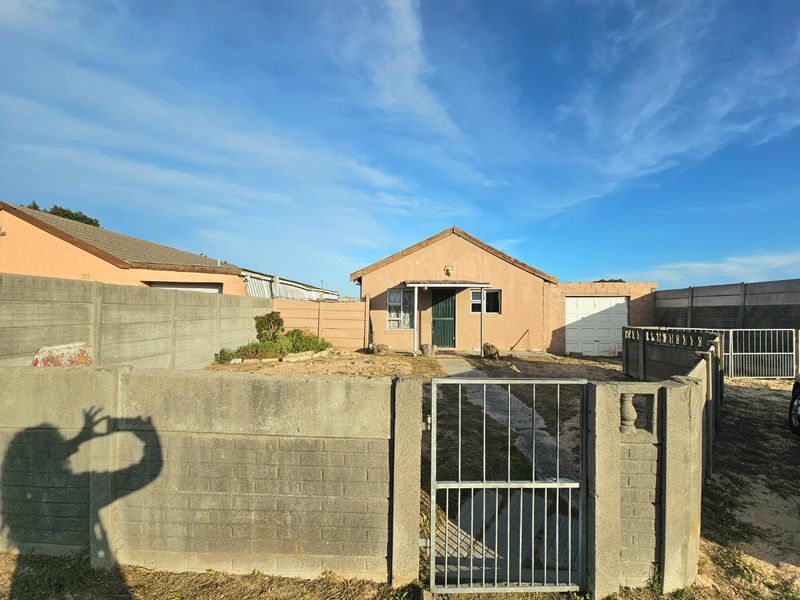 Front view of a detached house featuring a precast concrete boundary wall, metal gate, single garage, and a paved walkway leading to the entrance.