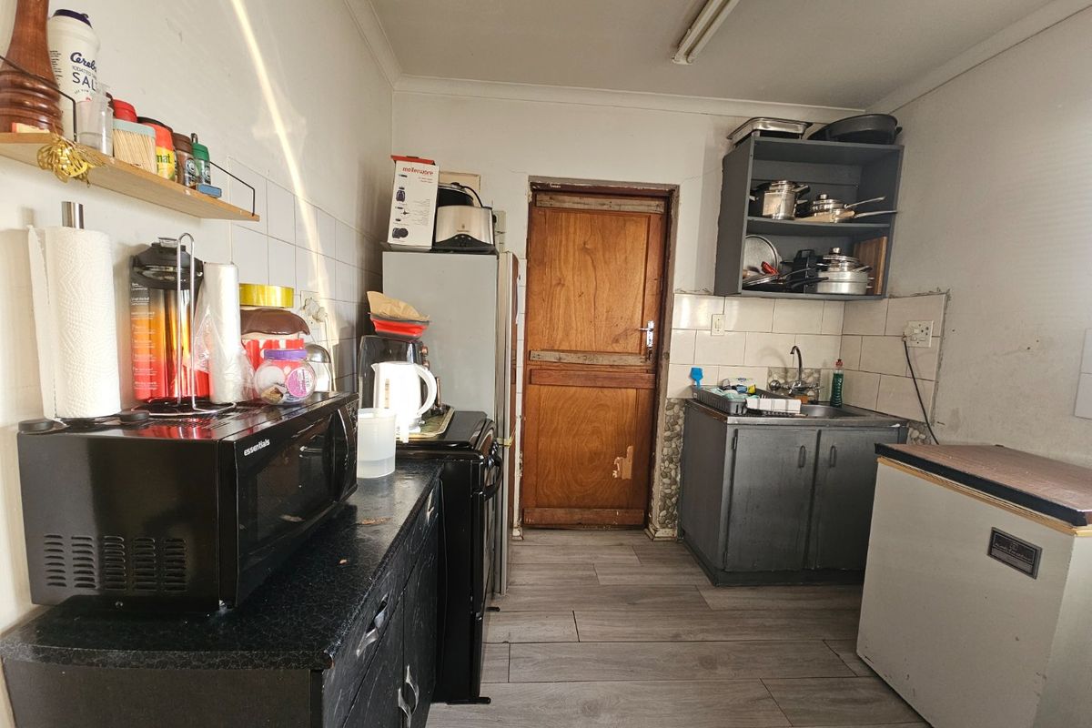 A functional kitchen space featuring built-in cabinetry, a sink, and tiled backsplash, currently requiring cosmetic updates and maintenance to improve its overall condition.