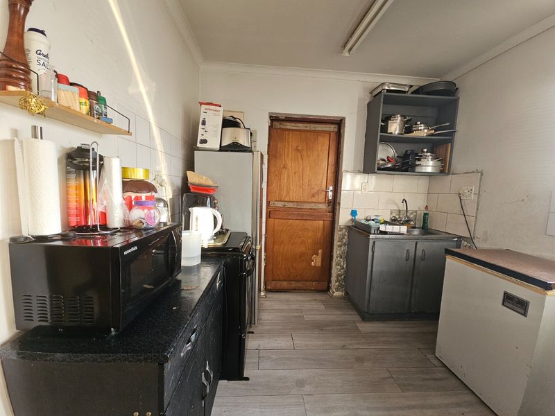 A functional kitchen space featuring built-in cabinetry, a sink, and tiled backsplash, currently requiring cosmetic updates and maintenance to improve its overall condition.