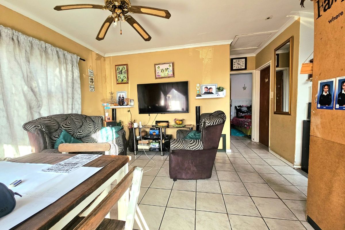 A living room featuring tiled flooring and a ceiling fan, with access to an adjacent bedroom.