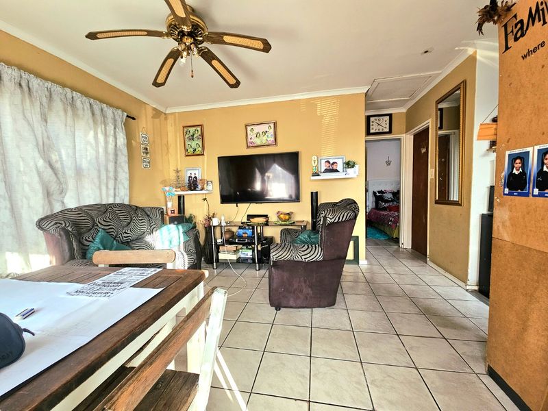 A living room featuring tiled flooring and a ceiling fan, with access to an adjacent bedroom.