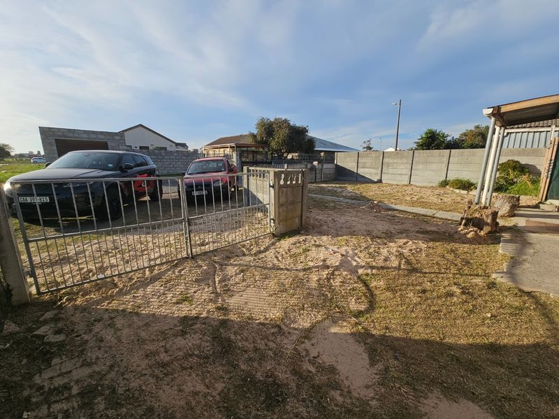 Front exterior view of the property featuring a metal driveway gate, concrete boundary walling, and an unlandscaped yard area.