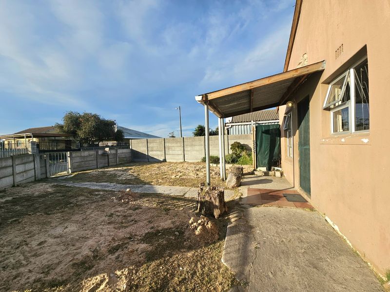 Rear exterior view of the property featuring a covered patio area, concrete boundary walls, and an open backyard space with potential for landscaping.
