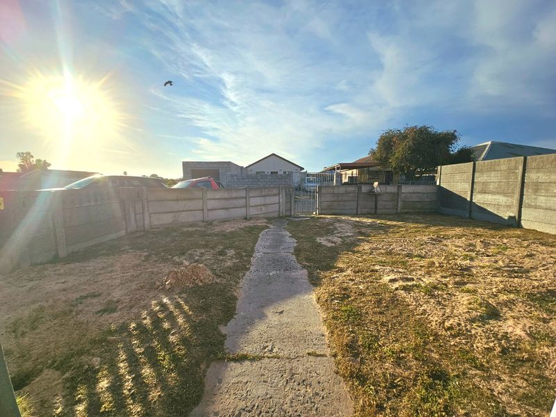 A rear garden area featuring a concrete pathway, enclosed by precast concrete boundary walls with a metal pedestrian gate.