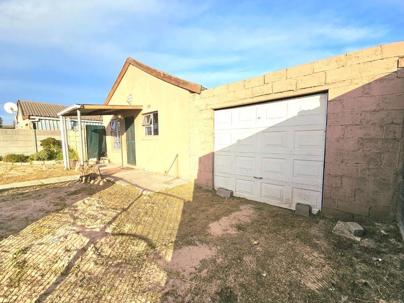 Rear view of the property featuring a single garage, covered patio area, and an unpaved garden space with perimeter walling.
