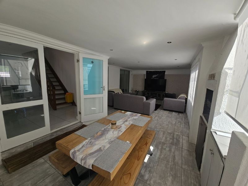 Spacious open-plan living and dining area featuring tiled flooring, recessed lighting, a built-in fireplace, and direct access to the staircase.