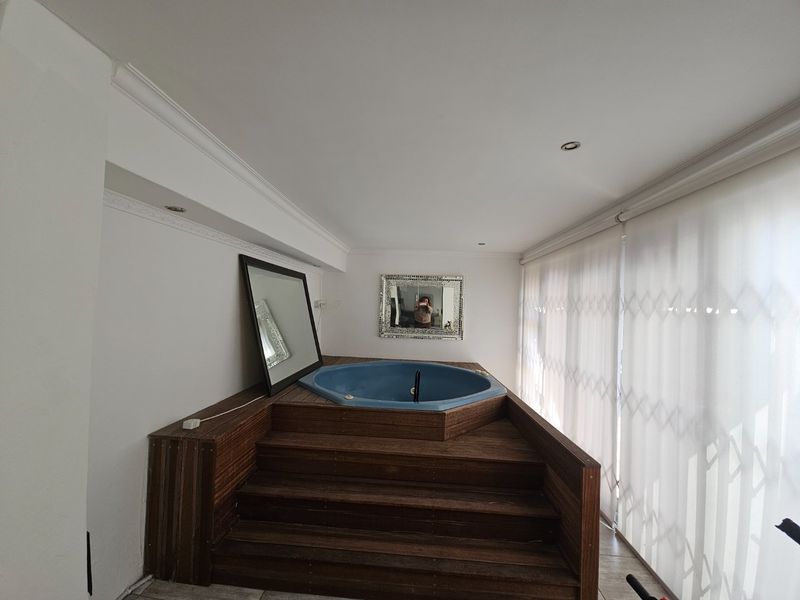 Indoor spa area featuring a built-in blue tub set within a raised timber deck, complemented by recessed lighting and large sliding glass doors.