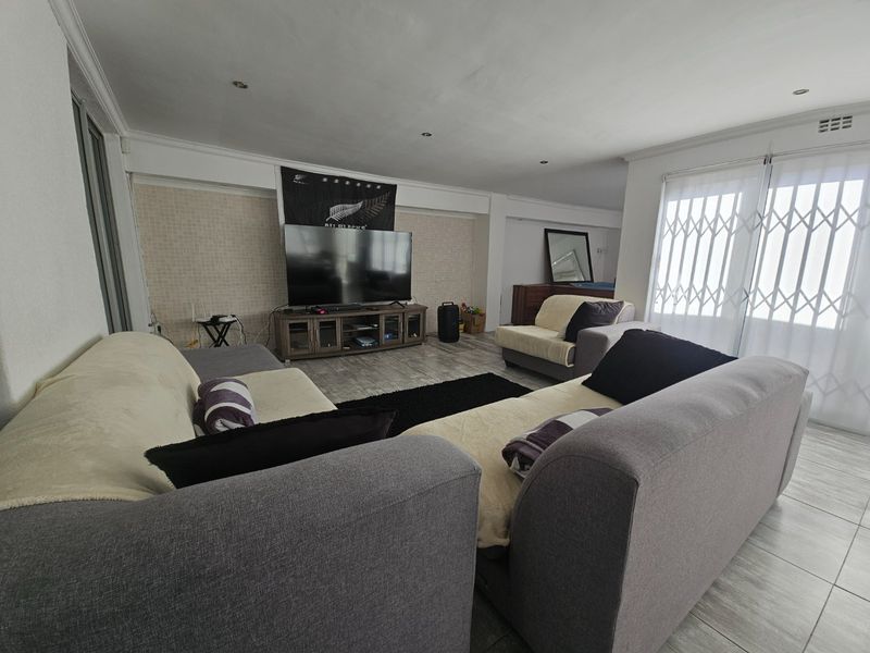 Spacious living room featuring tiled flooring, recessed downlighting, and a security gate, offering a comfortable and functional layout for relaxation.