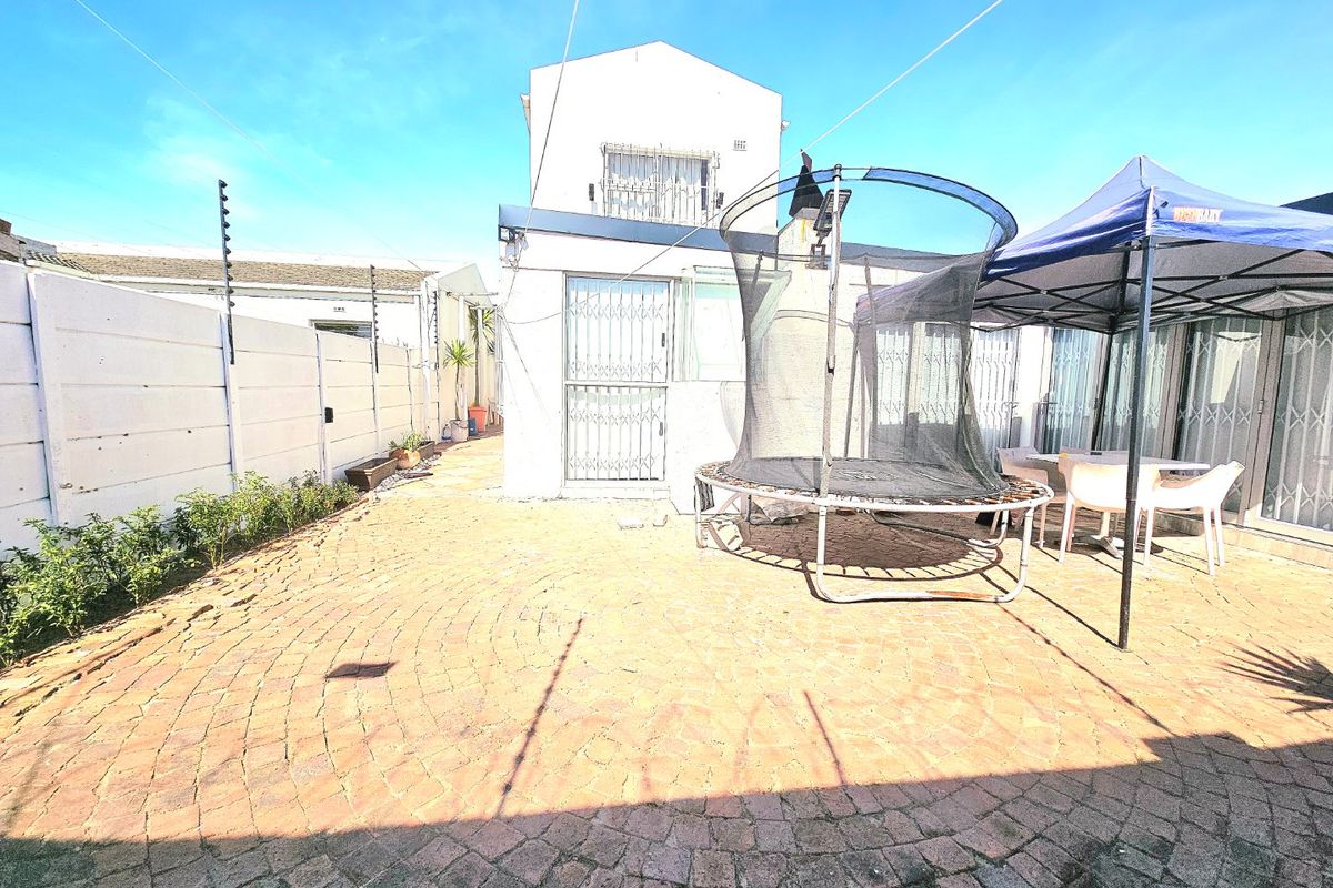 Rear exterior view featuring a paved patio area, secure perimeter wall with electric fencing, and access to the main dwelling via security gates.