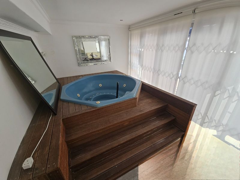 An indoor bathroom area featuring a built-in blue spa bath set within a raised timber deck, complemented by recessed lighting and large sliding doors.
