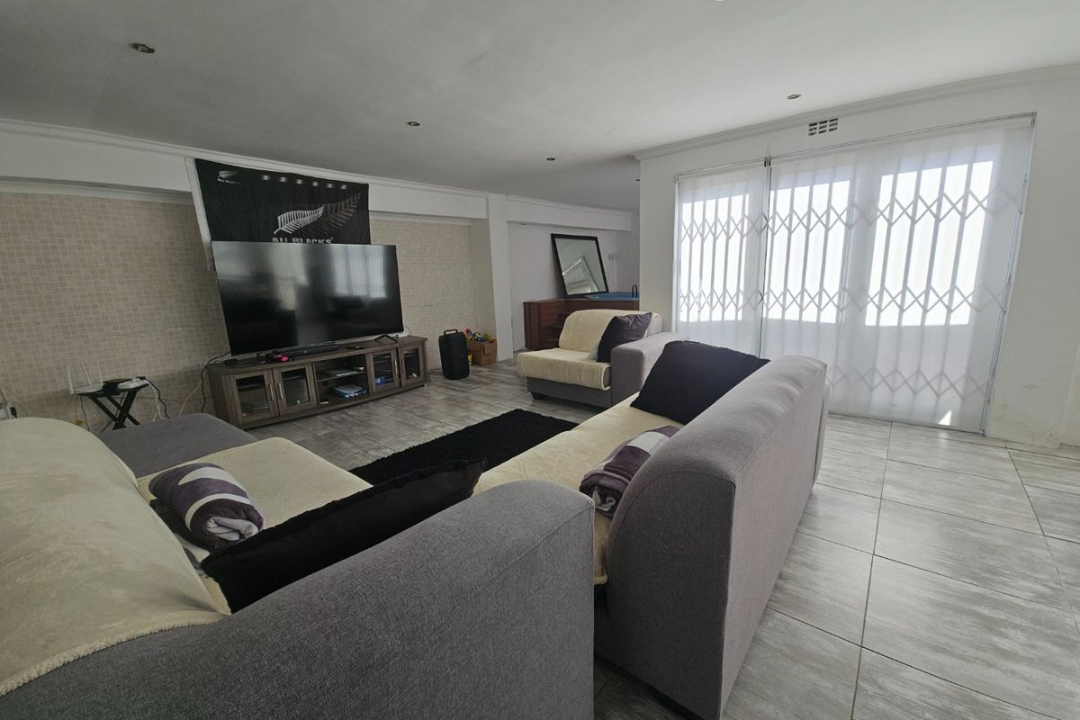 Spacious living room featuring tiled flooring, recessed lighting, and a sliding glass door with security gate, providing access to the exterior.