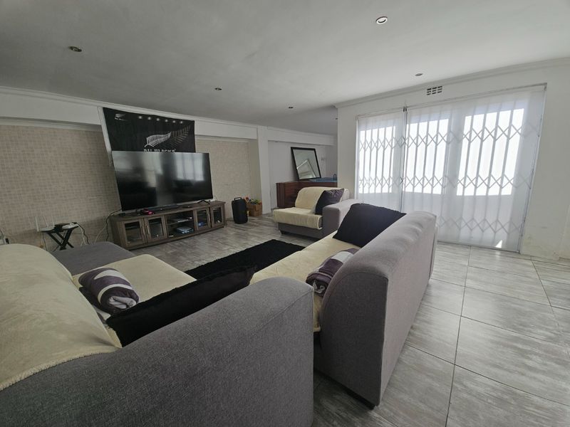 Spacious living room featuring tiled flooring, recessed lighting, and a sliding glass door with security gate, providing access to the exterior.