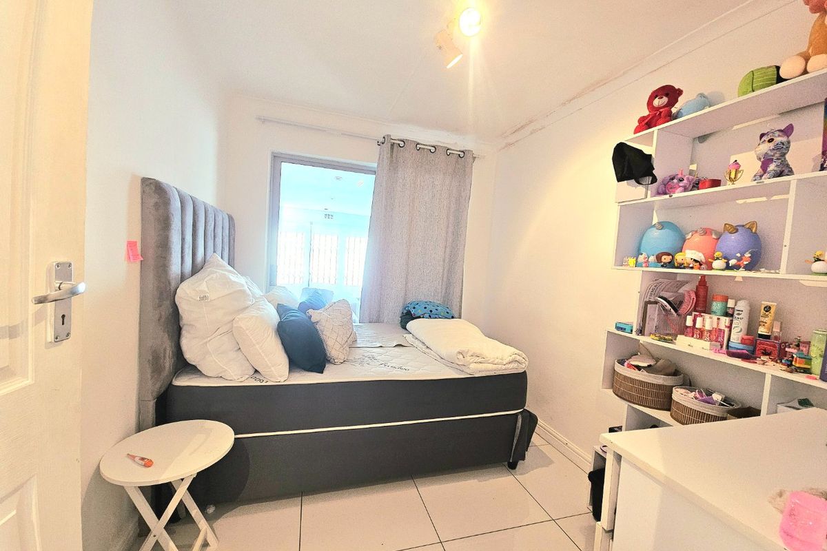 A compact bedroom featuring tiled flooring, a window with curtains, and built-in wall shelving.