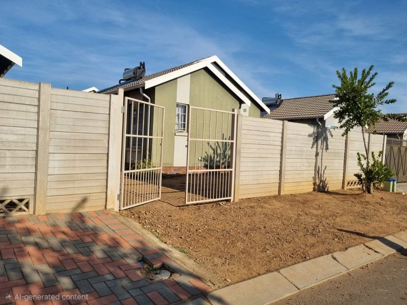 Front view of a residential property featuring a precast concrete boundary wall, metal entrance gate, paved driveway, and a solar geyser on the roof.