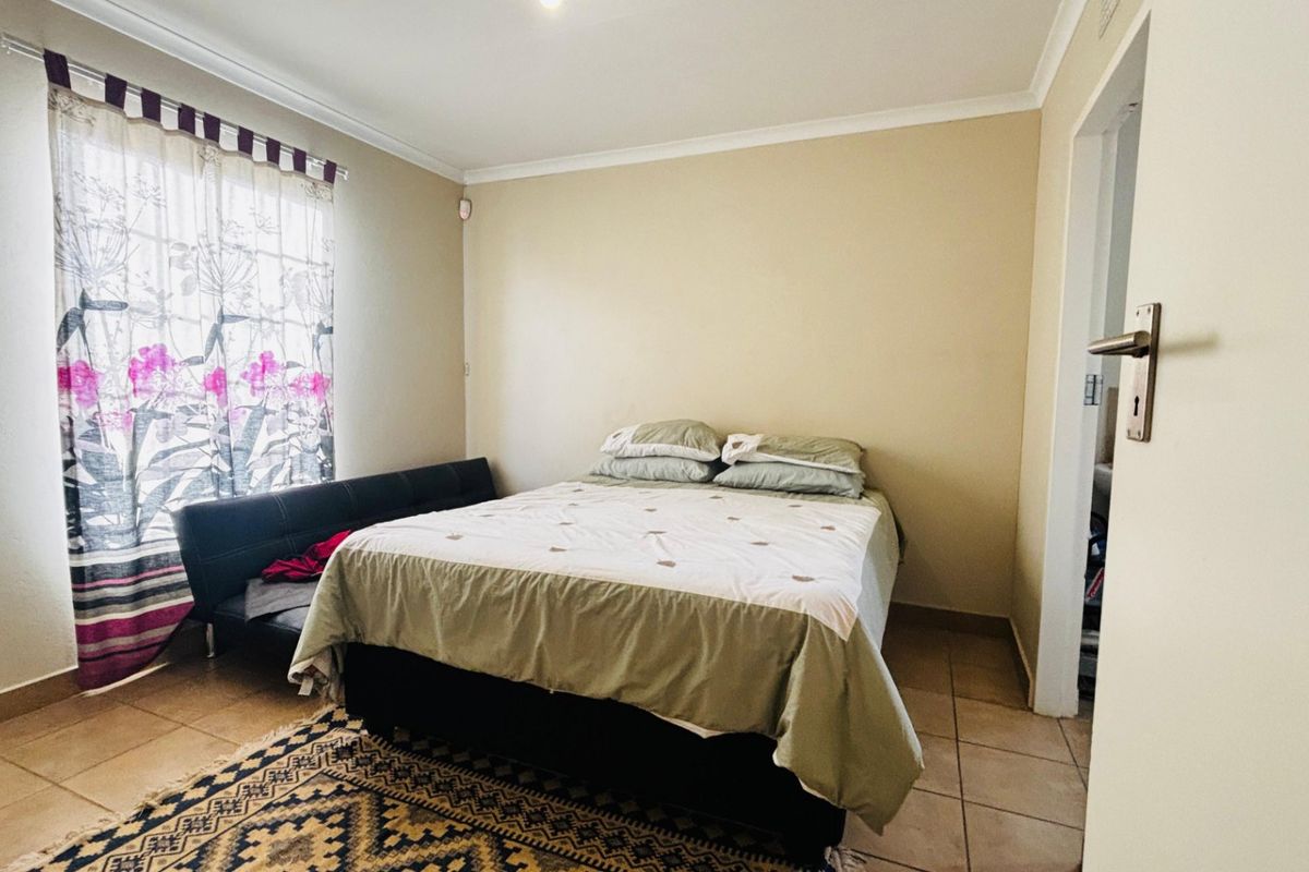 A functional bedroom featuring tiled flooring and neutral wall finishes, providing a comfortable and well-lit sleeping space.