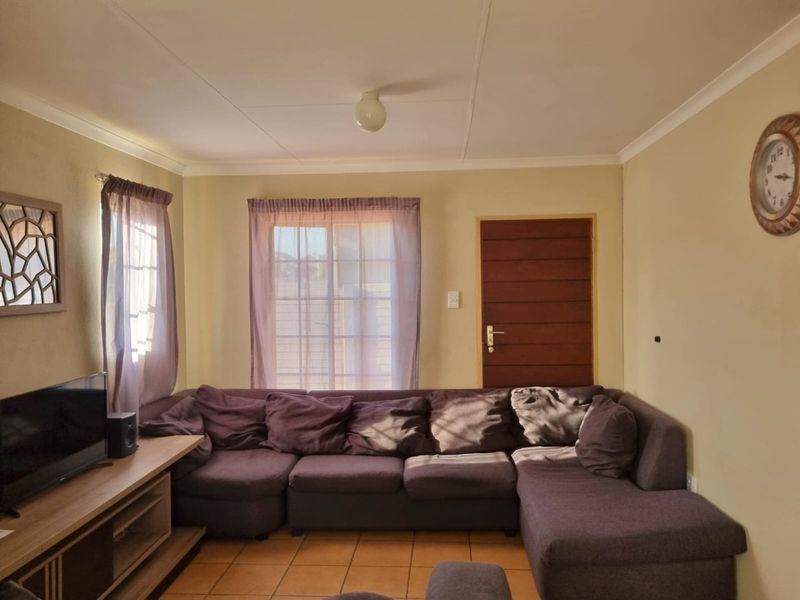 A functional living room featuring tiled flooring, a sliding glass door for natural light, and a solid timber door.