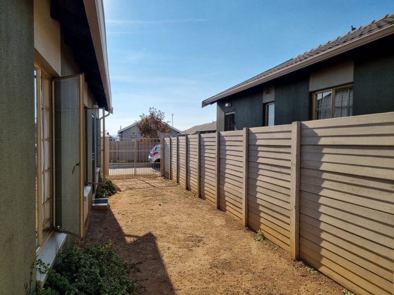 A side passage or rear yard area featuring a precast concrete boundary wall and metal security gate, providing access between property structures.