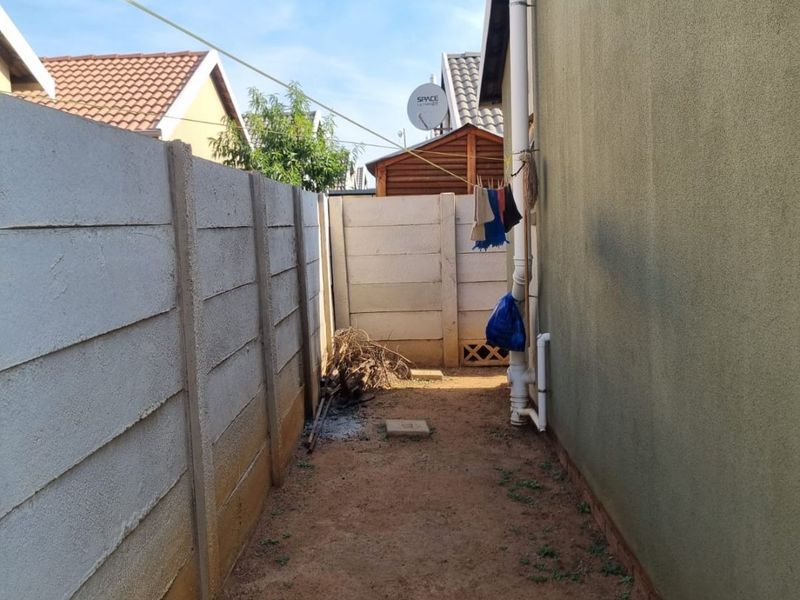 A narrow side passage featuring precast concrete boundary walls and exposed plumbing downpipes, requiring landscaping and surface improvements.