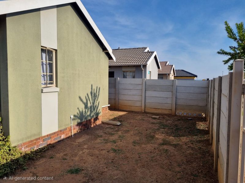 A view of the rear yard featuring a precast concrete boundary wall and the side elevation of the house with a tiled roof.