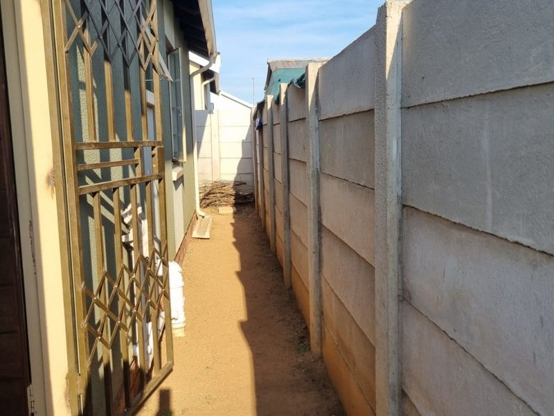 A narrow side passage featuring a precast concrete boundary wall and a metal security gate leading to the property entrance.