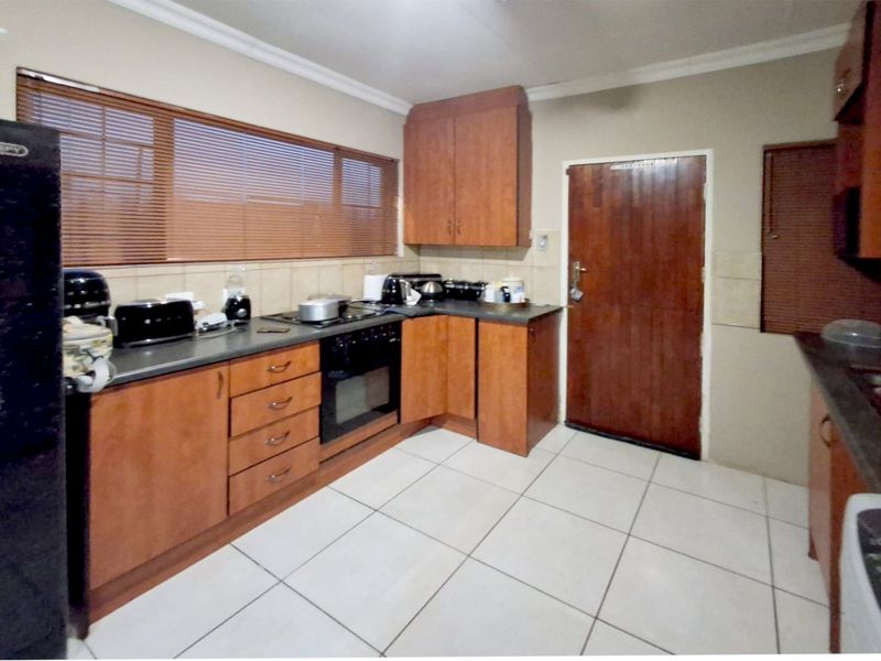 A functional kitchen featuring wooden cabinetry, dark countertops, built-in oven and hob, tiled flooring, and natural light through venetian blinds.