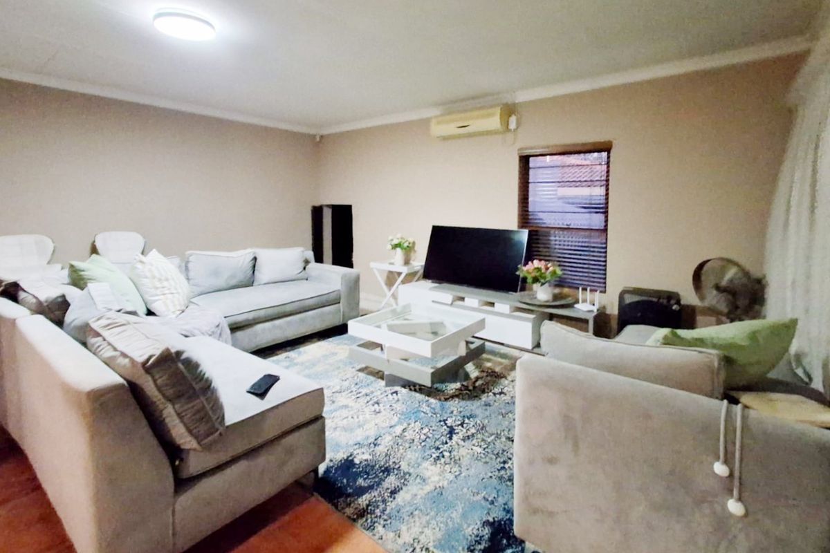 A comfortable living room featuring tiled flooring, a wall-mounted air conditioning unit, and a window with fitted blinds.