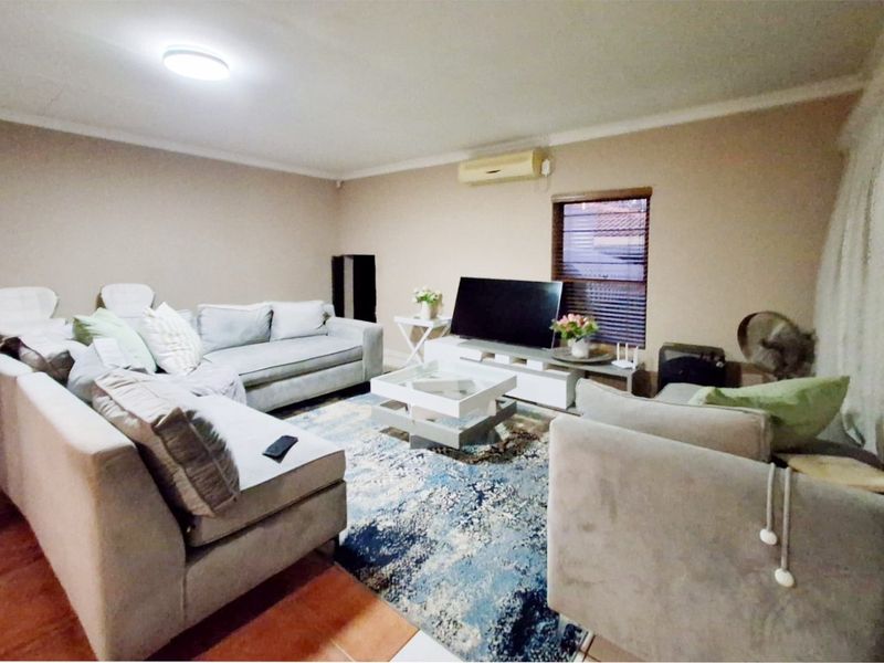 A comfortable living room featuring tiled flooring, a wall-mounted air conditioning unit, and a window with fitted blinds.